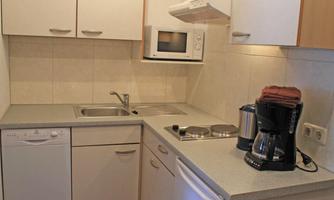 A modern kitchen with a sink, stove, and microwave. On the side, there is a coffee machine and a dishwasher is also available.