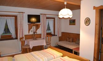 A cozy room with two beds and simple wooden decor. There is a table, chairs, and a window with curtains.