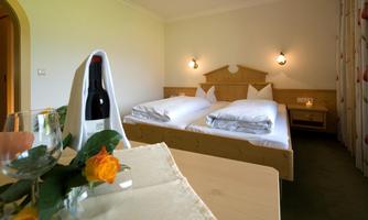 A cozy room with two beds and stylish decor. On the table is a bottle of wine and some fresh flowers.