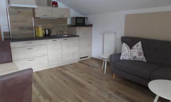 A cozy living kitchen with modern furniture and wooden floors. The room includes a kitchenette, a dining table, and a sofa.