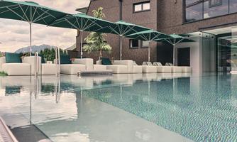 A modern pool with smooth water and sun umbrellas. In the background, there is a stylish house with large windows.
