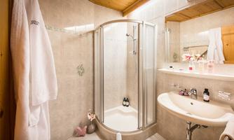 A modern bathroom with a shower and a sink. In the background, personal care products and a bathrobe can be seen.