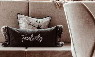Two decorative cushions on a couch. One has a stylized deer, the other features the inscription "Laziness."