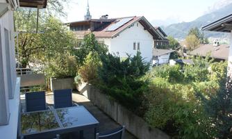 A well-kept outdoor area with a table and chairs. In the background, green plants and residential buildings can be seen.