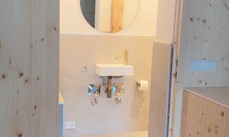 A modern bathroom with a round mirror and a white sink. The walls are light and made of wood, creating a cozy atmosphere.