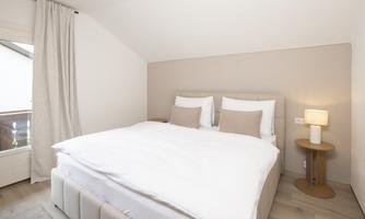 A modern bedroom with a large bed and bright walls. Next to the bed is a small lamp and there is a window with curtains.