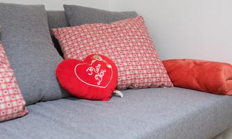 A cozy sofa with gray upholstery and decorative cushions. A red heart-shaped cushion with the inscription "I love you" adds a romantic touch.