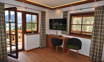 A cozy room with wooden details, large windows, and a desk. In the background, there is a television, and the view of the mountains is visible.