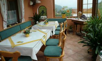 A cozy conservatory with a large table and chairs. Green plants and sunny windows create a warm atmosphere.