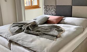 A cozy bedroom with an elegant bed and decorative pillows. A warm atmosphere is created by the windows and soft textiles.