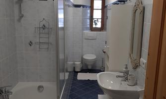 A modern bathroom with a bathtub and a shower. The walls are light tiled, and there is plenty of daylight coming through the window.
