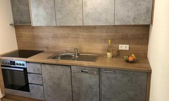 A modern kitchen with gray cabinets and a wood surface. On the countertop, there is a bottle of wine and a bowl of fruit.