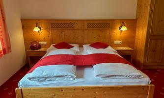 A cozy bedroom with a wooden bed and red pillows. The walls are painted in warm colors and there is a wooden dresser.