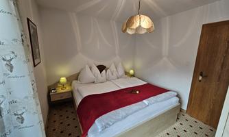 A cozy bedroom with a double bed and white pillows. A red throw on the bed and soft lighting create an inviting atmosphere.