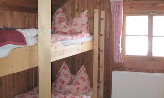 A cozy wooden accommodation with bunk beds and colorful pillows. The room has a window that lets in natural light.