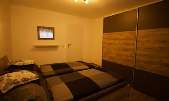 A simple bedroom with two beds and neutral colors.  
On the wall, there is a small mirror and a closed wardrobe.