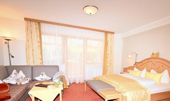 A modern hotel room with a comfortable double bed and a cozy seating area. Large windows provide plenty of natural light.