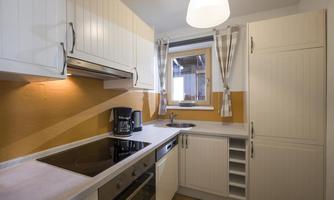 A modern kitchen with white cabinets and a light wall color. It is equipped with a stove, a sink, and a window that lets in natural light.