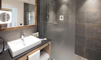 A modern bathroom with a glass shower and an elegant sink. The walls are clad with dark tiles.