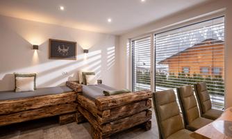 A modern room with wooden furniture and large windows. The space is bright and inviting, with a dining area and a view of the outdoor landscape.