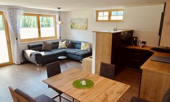 A modern living room with a cozy sofa and a dining table.  
Large windows let in plenty of light and the kitchen is well equipped.