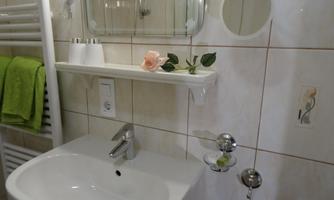 A modern bathroom with a white sink and a large mirror. On the shelf, there is a flower and some towels in vibrant green.