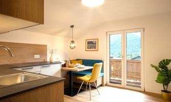 A modern kitchen with a cozy dining area and a balcony. Bright colors and large windows create an inviting atmosphere.