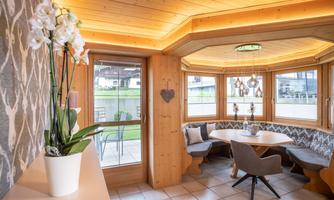 A cozy dining area with a large window front and wood paneling. The decor is modern and bright, with a beautiful orchid as decoration.