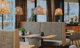 A cozy restaurant with modern benches and warm lighting. Large windows provide a view outside and create an inviting atmosphere.