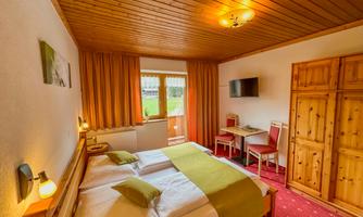 A cozy bedroom with two beds, wooden paneling, and a small balcony. There is a desk and a television mounted on the wall.