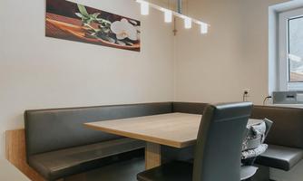 A modern dining room with a cozy seating area and a wooden table. A decorative picture of flowers hangs on the wall.