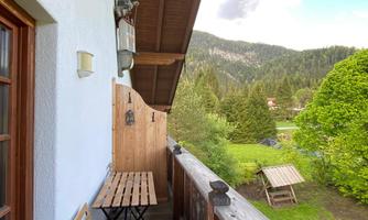 A cozy balcony with a small table and two chairs. In the background, green trees and rolling landscapes are visible.