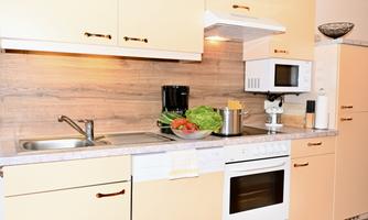 A modern kitchen with bright cabinets and a countertop. Fresh vegetables are on the side, while the kitchen appliances are well organized.