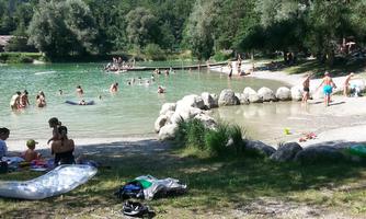A beautiful swimming lake surrounded by trees and mountains. Many people enjoy the water on a sunny day.