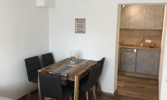 A dining area with a wooden table and black chairs. The kitchen is open and modern in design.