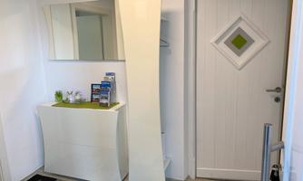 A bright hallway with a modern, white wardrobe and a mirror. On the wall hangs a door with a diamond-shaped window.