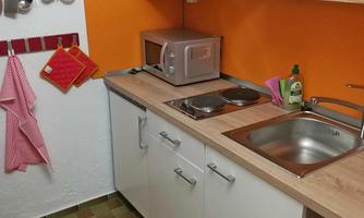 A modern kitchen with wooden surfaces and orange walls. There is a stove, a sink, and some kitchen appliances.
