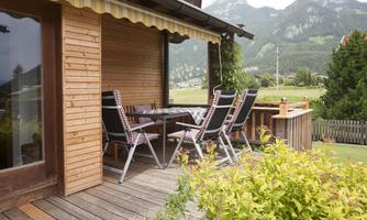 A cozy terrace with a wooden table and chairs. The view of the mountains and the green landscape is impressive.