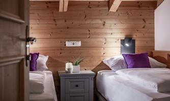 A cozy bedroom with two single beds and wood paneling. A small plant sits on the nightstand and there are purple pillows on the beds.