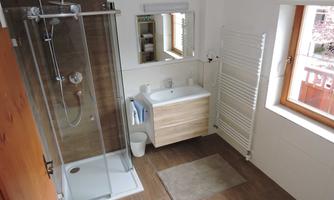 A modern bathroom with a shower, a sink, and a large mirror. The walls are light, and there is a window that lets in daylight.