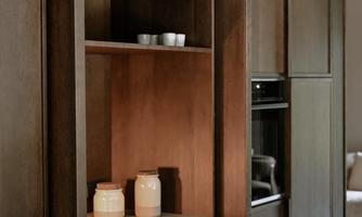 A modern kitchen with dark wood and open shelves. Various decorative vessels and dishes are on the shelves.