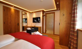 A modern bedroom with wooden paneling and a large window. The decor is simple and elegant, featuring a red duvet and a TV.