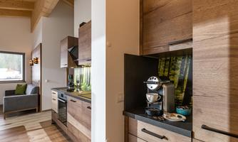 A modern kitchen with wooden furniture and an open living area. There is a coffee machine and a relaxing atmosphere.