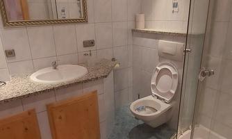 A modern bathroom with a shower and sink. There are bright tiles and wooden paneling visible.
