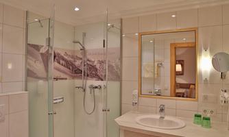 A modern bathroom with a glass shower and a large mirror. The walls are brightly tiled and there is an appealing mountain landscape in the background.