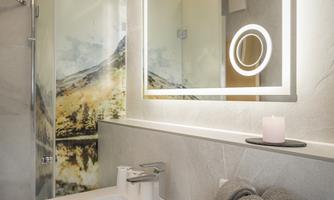 A modern bathroom with an elegant sink and a lit mirror. In the background, there is a wall featuring an inspiring landscape graphic.