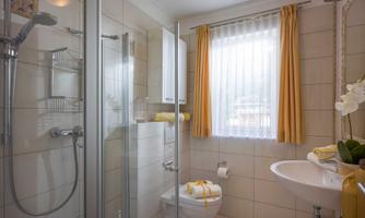 A modern bathroom with a shower and bright tiles. The curtains are yellow, and there are fresh towels on the sink.