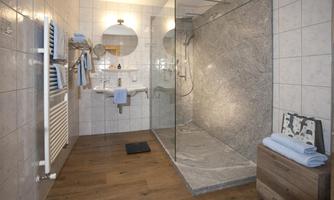 A modern bathroom with a glass shower and tiled walls. The floor has a wooden floor, and various towels are neatly arranged.