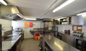 A modern kitchen with stainless steel fixtures and multiple cooktops. The walls are brightly tiled, and there are some utensils on the shelves.