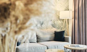 A stylish living room with a gray sofa and a modern floor lamp. In the foreground, you can see decorative dried flowers and a table with a magazine.